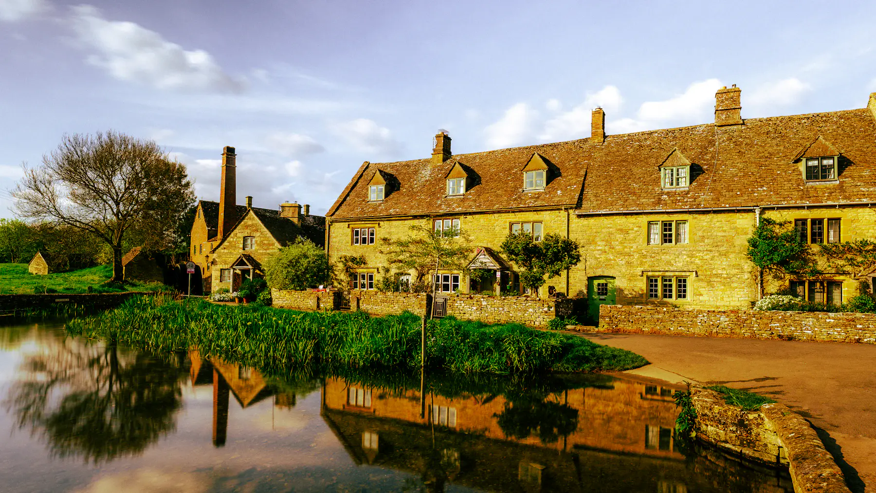 Historic stone cottages reflected in a quiet village pond