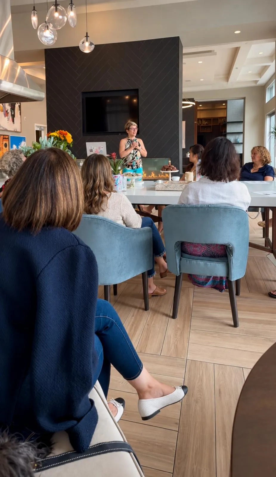 Mehri speaking to guests seated around a long table in front of a fireplace