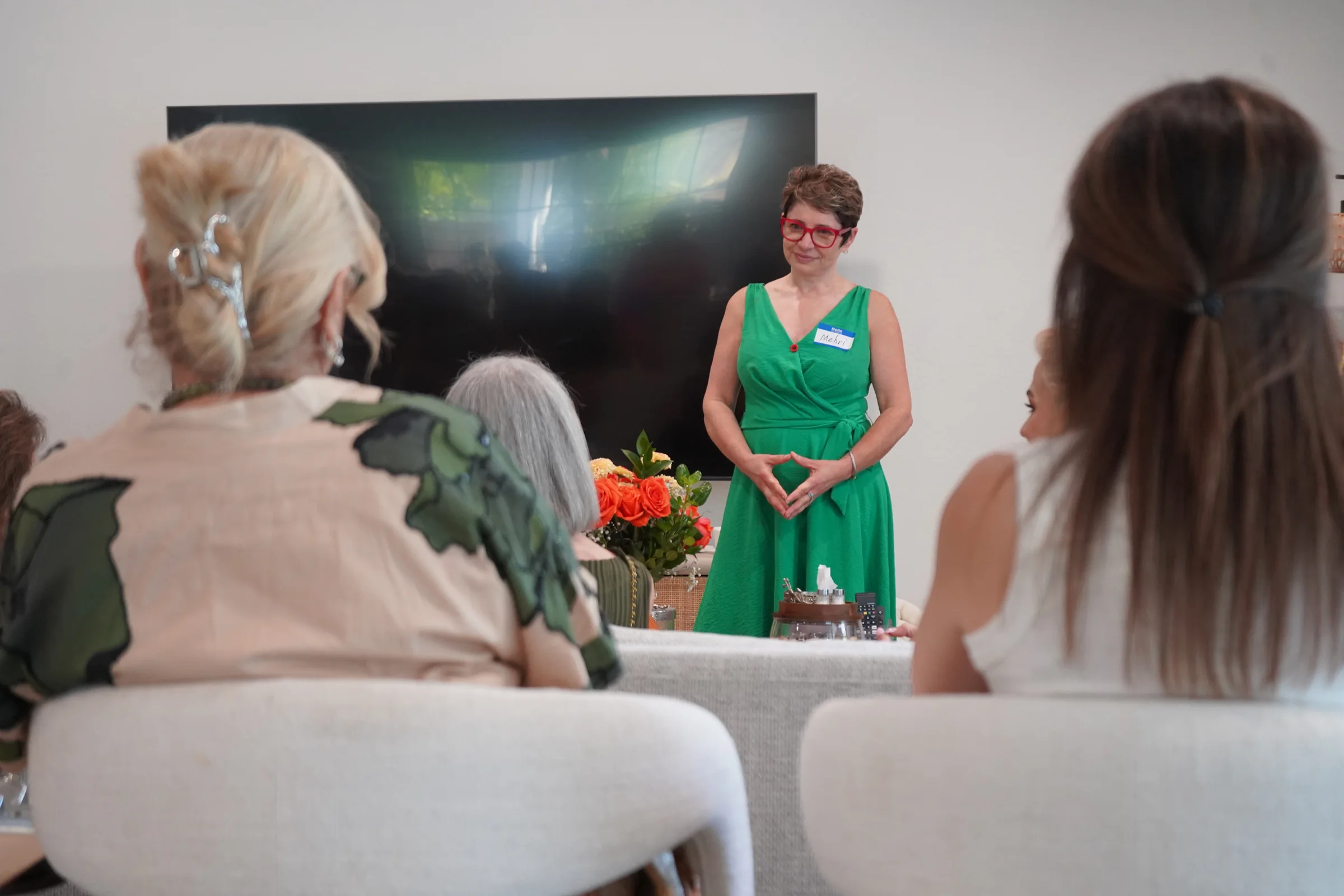 The host in green speaks with guests seated in a circle
